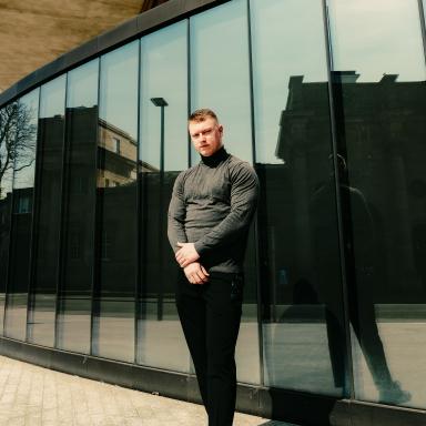 Samuel outside in front of a large mirrored window